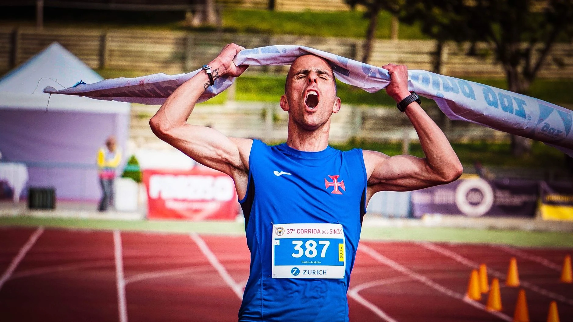 Atlet slaví vítězství na cílové čáře maratonu, triumfálně zvedající pásku nad hlavou.