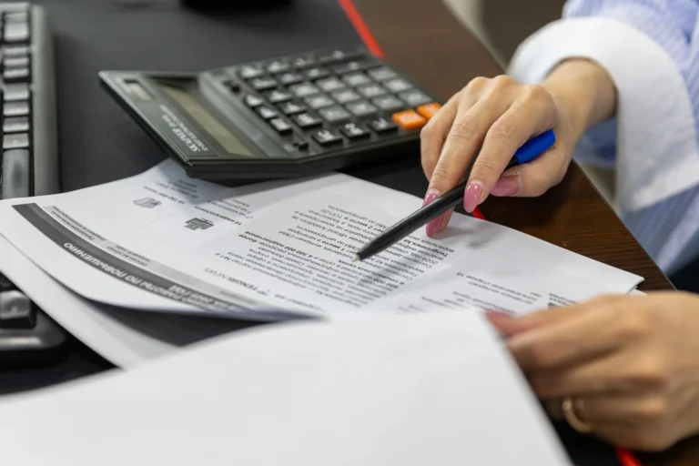 Detail ženské ruky prohlížející finanční dokumenty pomocí kalkulačky.