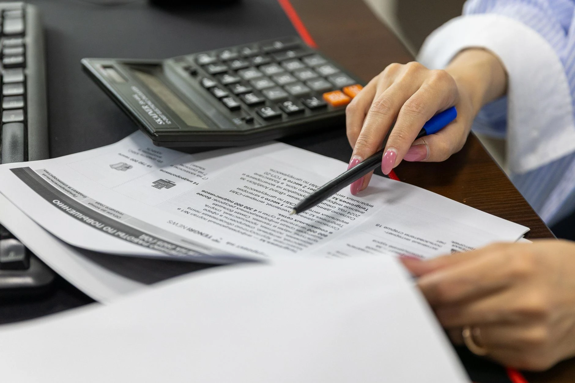 Detail ženské ruky prohlížející finanční dokumenty pomocí kalkulačky.