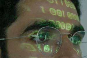 Detailní snímek osoby, na jejíž brýle je promítán binární kód, symbolizující digitální technologie.