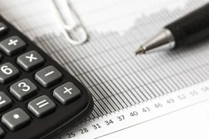 Detailní záběr kalkulačky a pera na sloupcovém grafu, představující finance a účetnictví.