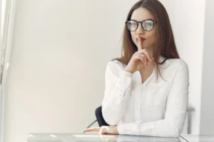 Elegantní podnikatelka naznačuje ticho prstem na rtech v moderním kancelářském prostředí.