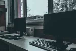Prázdné kancelářské pracovní místo se dvěma počítačovými monitory u okna, vyjadřující moderní a profesionální prostředí.