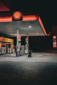 Slabě osvětlená benzínka Shell s motocyklem zaparkovaným pod jasnými světly během noci.