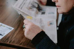 Žena čte noviny u dřevěného stolu, zaměřuje se na odpočinek a informace.