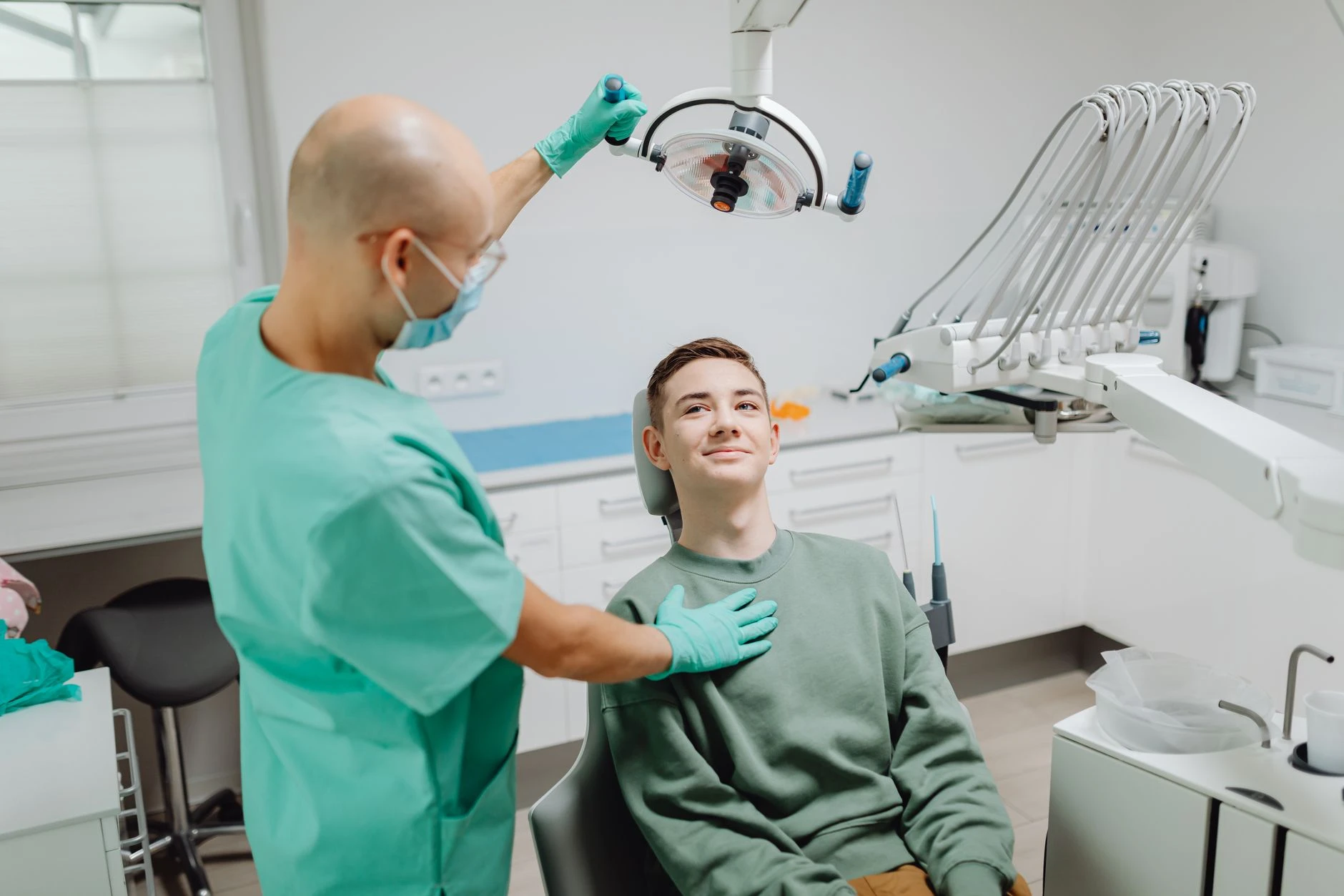 Zubař vyšetřuje pacienta pod stomatologickým světlem v moderním klinickém prostředí.